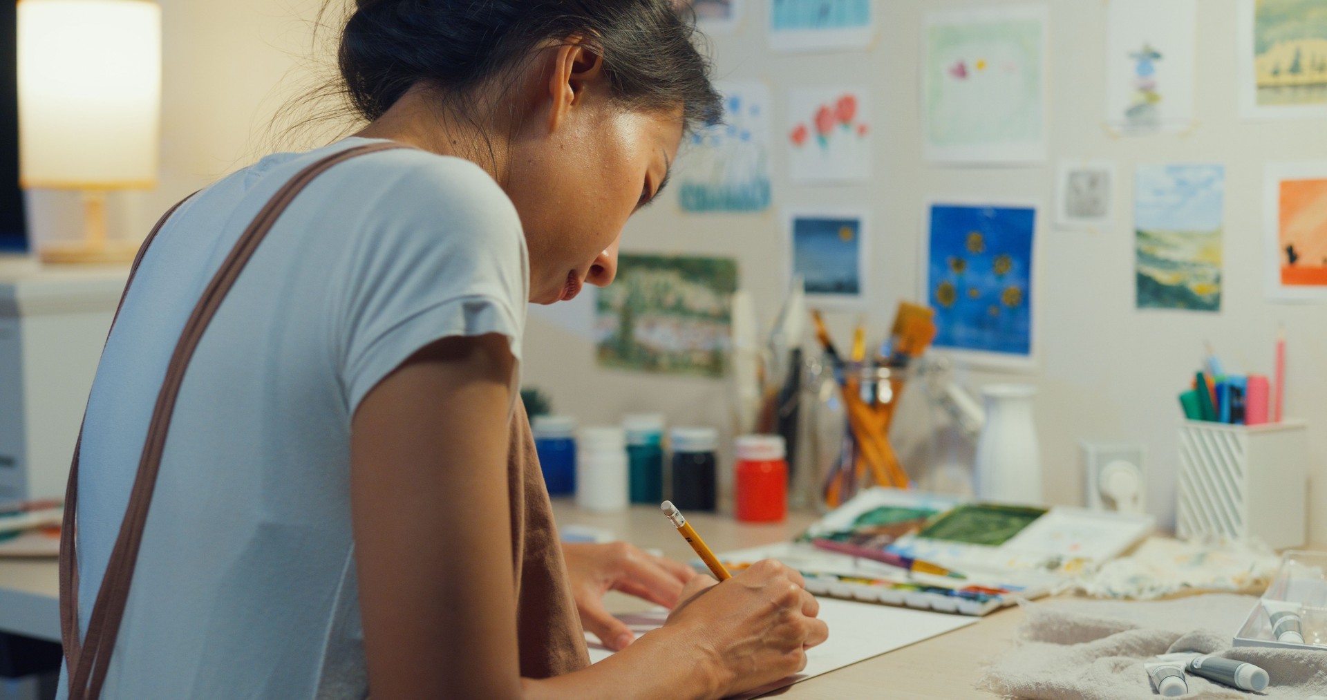 Youth Asia lady wear apron sit front of desk drawing picture on sketchbook create artwork cozy workshop in home at night. Contemporary Painter Abstract Modern Art, Creativity and people.